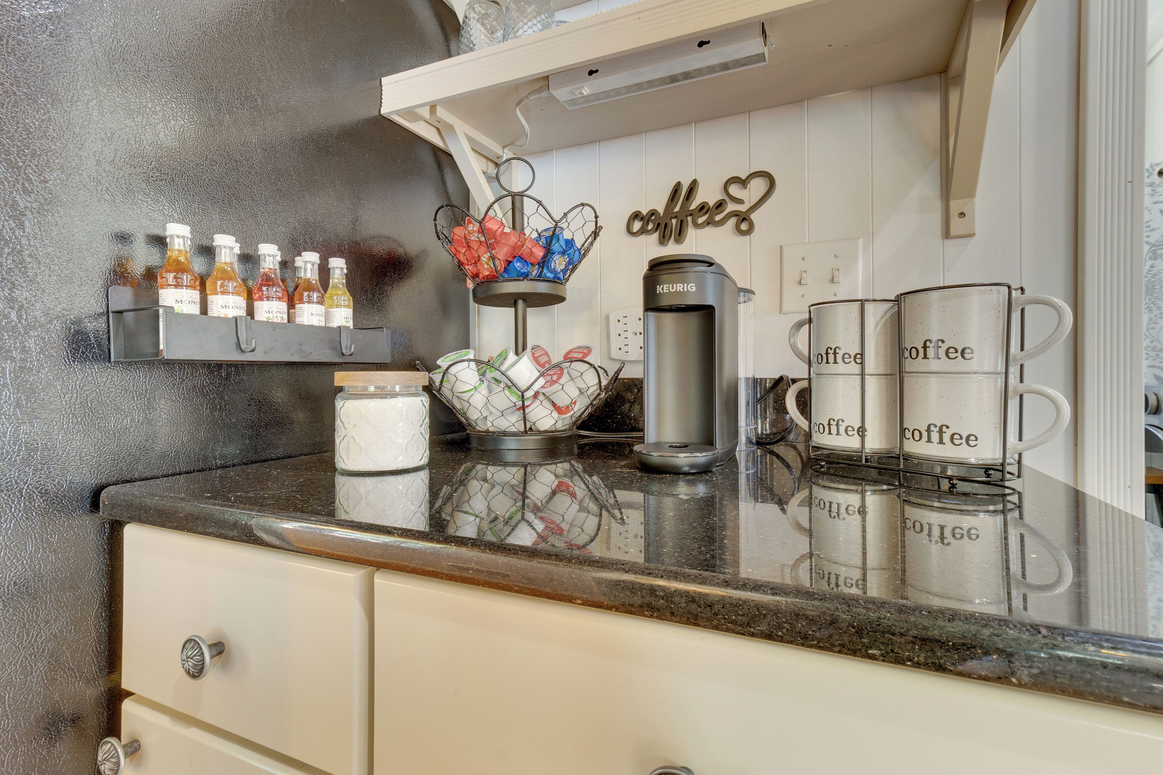 Una encimera de cocina con una estación de café, que incluye una cafetera Keurig, tazas de café y una cesta con sobres de café.