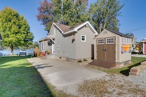A two-story house with a garage and a small shed, surrounded by trees and a body of water.