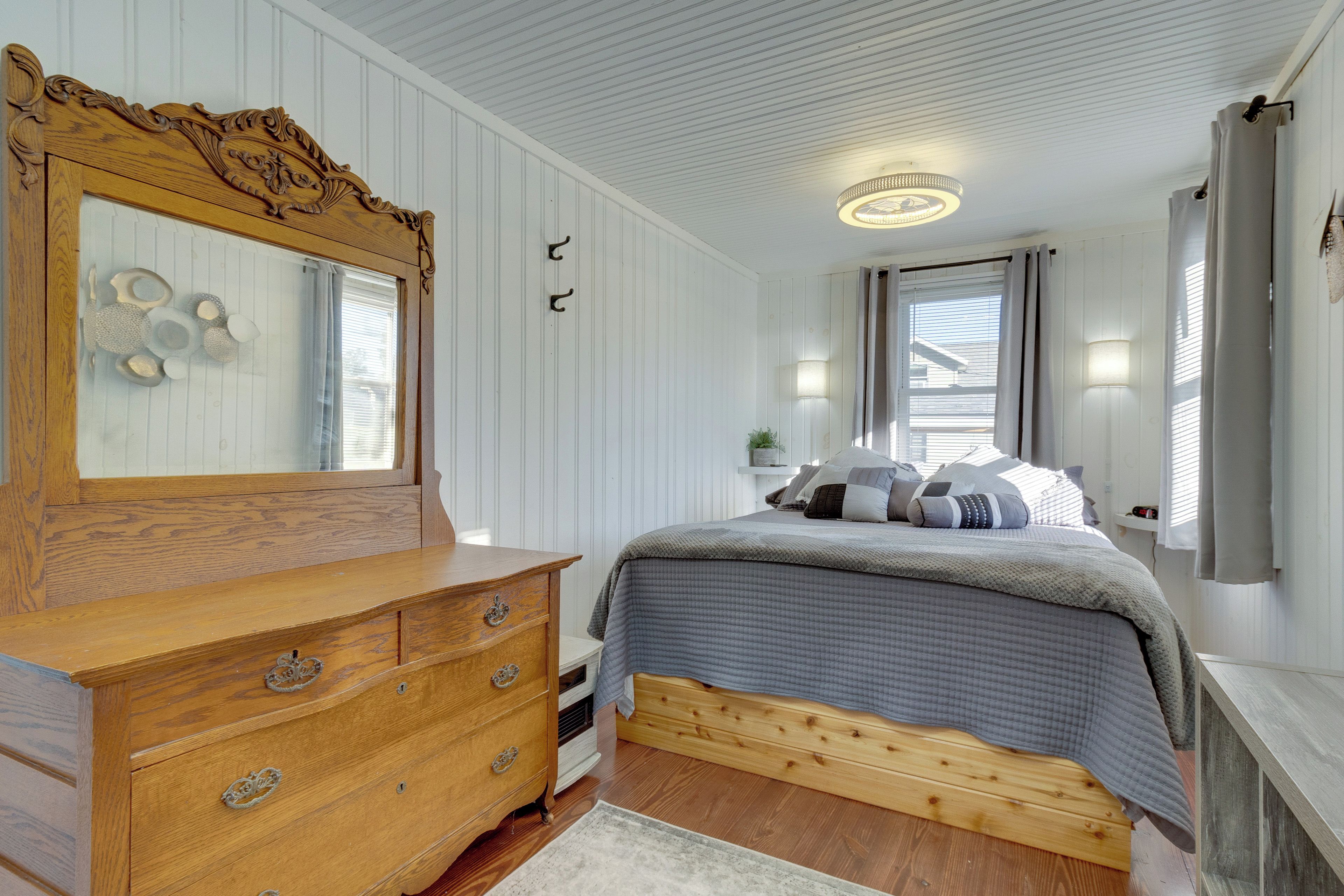 A bedroom with a wooden dresser, a bed with a quilted cover, a mirror with decorative carvings, and a ceiling light fixture.