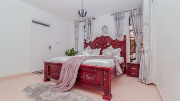Quarto com estrutura de cama vermelha, roupa de cama branca, tapete fofo e uma planta.