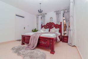 Quarto com estrutura de cama vermelha, roupa de cama branca, tapete fofo e uma planta.