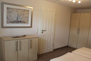 Een slaapkamer met een bed, een kledingkast, een deur en een lijst met een afbeelding aan de muur.