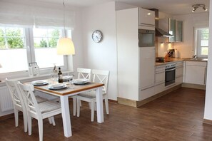 Uma cozinha moderna com armários brancos, forno embutido e um espaço de jantar com mesa de madeira e cadeiras brancas.