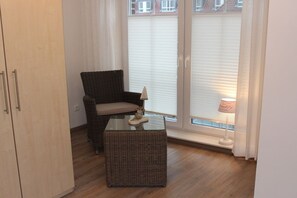 A room with a wicker chair, a small table, and a lamp. - Holiday home with 2 bedrooms (Greetsiel)