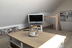 Een kamer met een televisie op een standaard, een glazen pot met een touwhandvat op een houten tafel en een fotolijst met een nautisch thema.