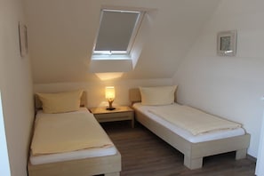 A small, single-room apartment with two beds, a skylight, and a nightstand with a lamp. - Holiday home with 2 bedrooms (Greetsiel)