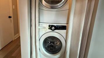 A laundry room with a stacked washer and dryer, wooden flooring, and a door leading to another room.