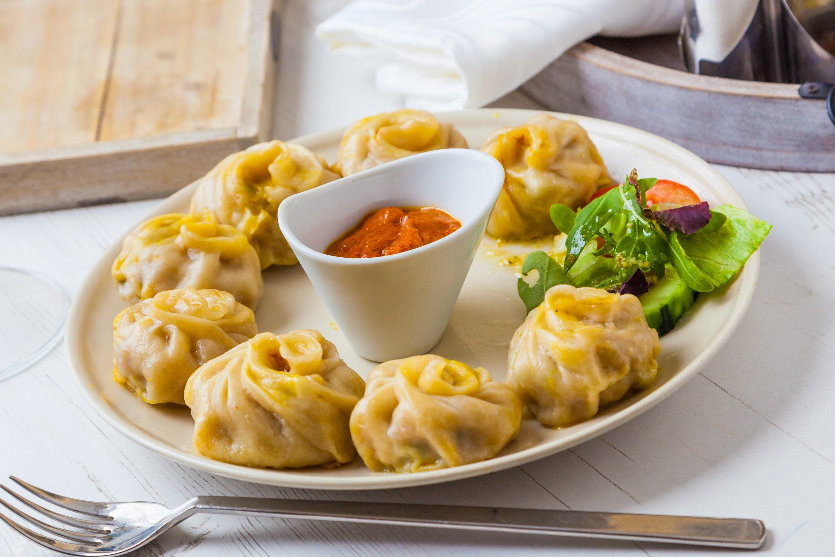 A plate of dumplings with a side of salad and a dipping sauce.