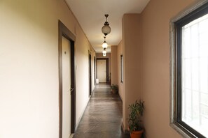 Um corredor com piso de mármore, portas à esquerda e plantas em vasos à direita.