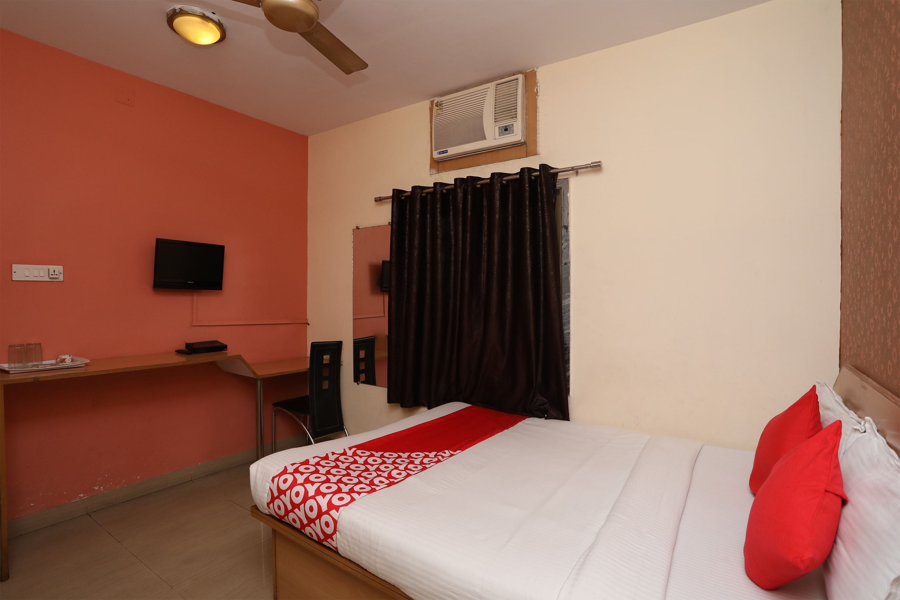 A bedroom with a bed, a desk, a chair, a television, and a window with curtains.