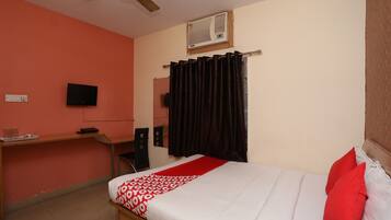 A bedroom with a bed, a desk, a chair, a television, and a window with curtains.