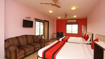 A hotel room with a sofa, two beds, a television, ceiling fans, and an air conditioning unit.
