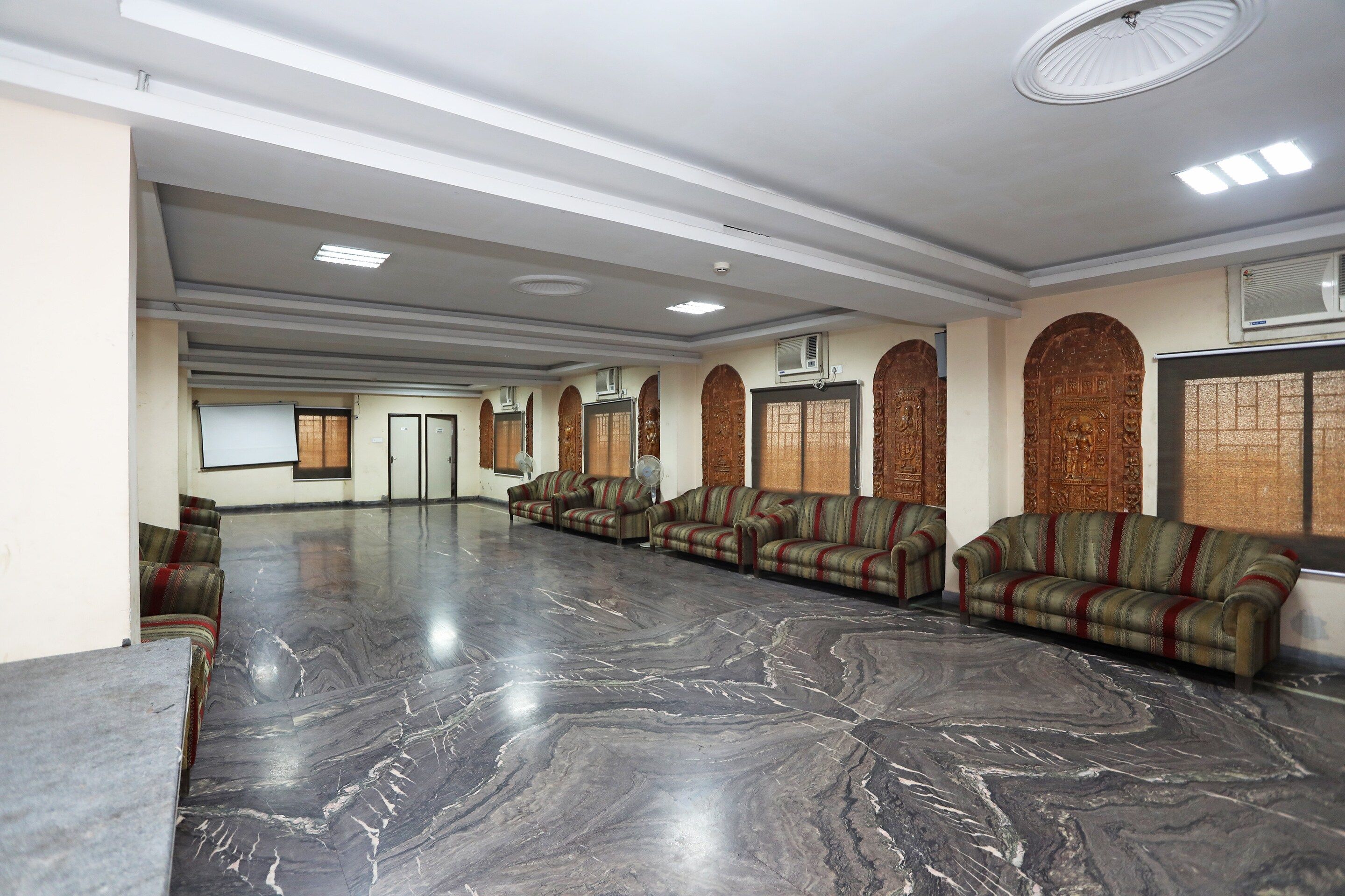 A spacious hall with a polished marble floor, rows of sofas, and a large whiteboard on the left.