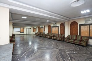 A spacious hall with a polished marble floor, rows of sofas, and a large whiteboard on the left.