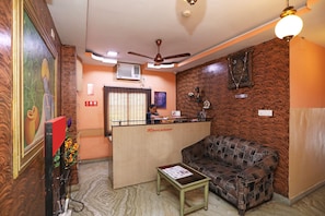 Uma área de recepção com balcão, sofá, mesa pequena e ventilador de teto.