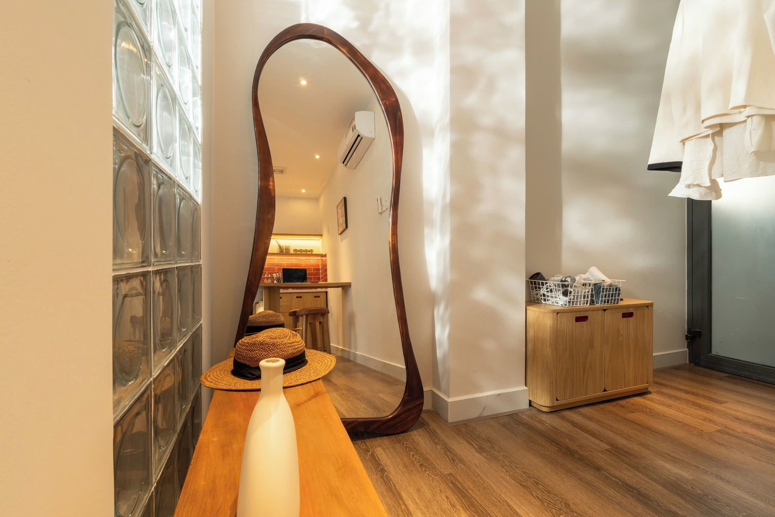 A room with a wooden floor, a large mirror, a woven basket, and a wooden cabinet with laundry baskets.