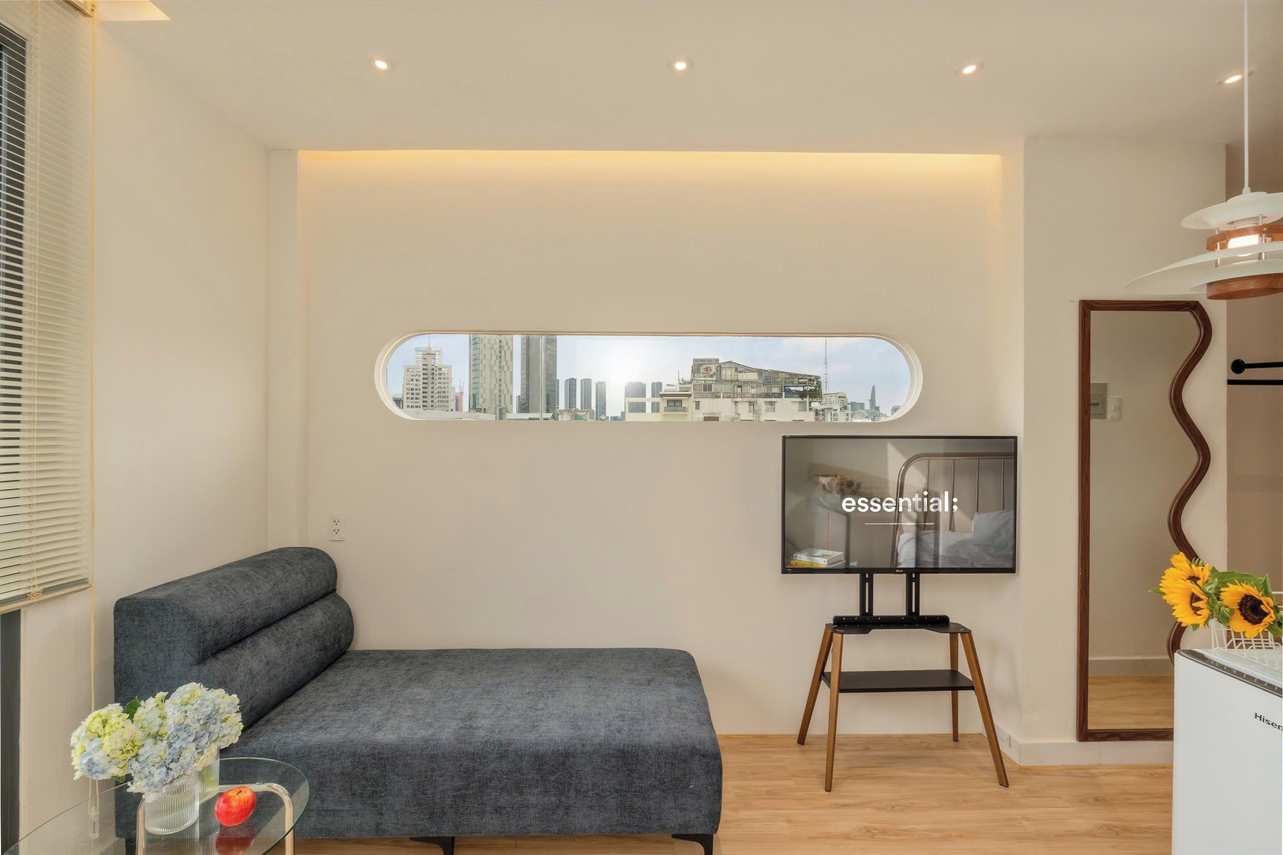 A modern living room with a grey sofa, a flat-screen TV mounted on the wall, and a cityscape view.