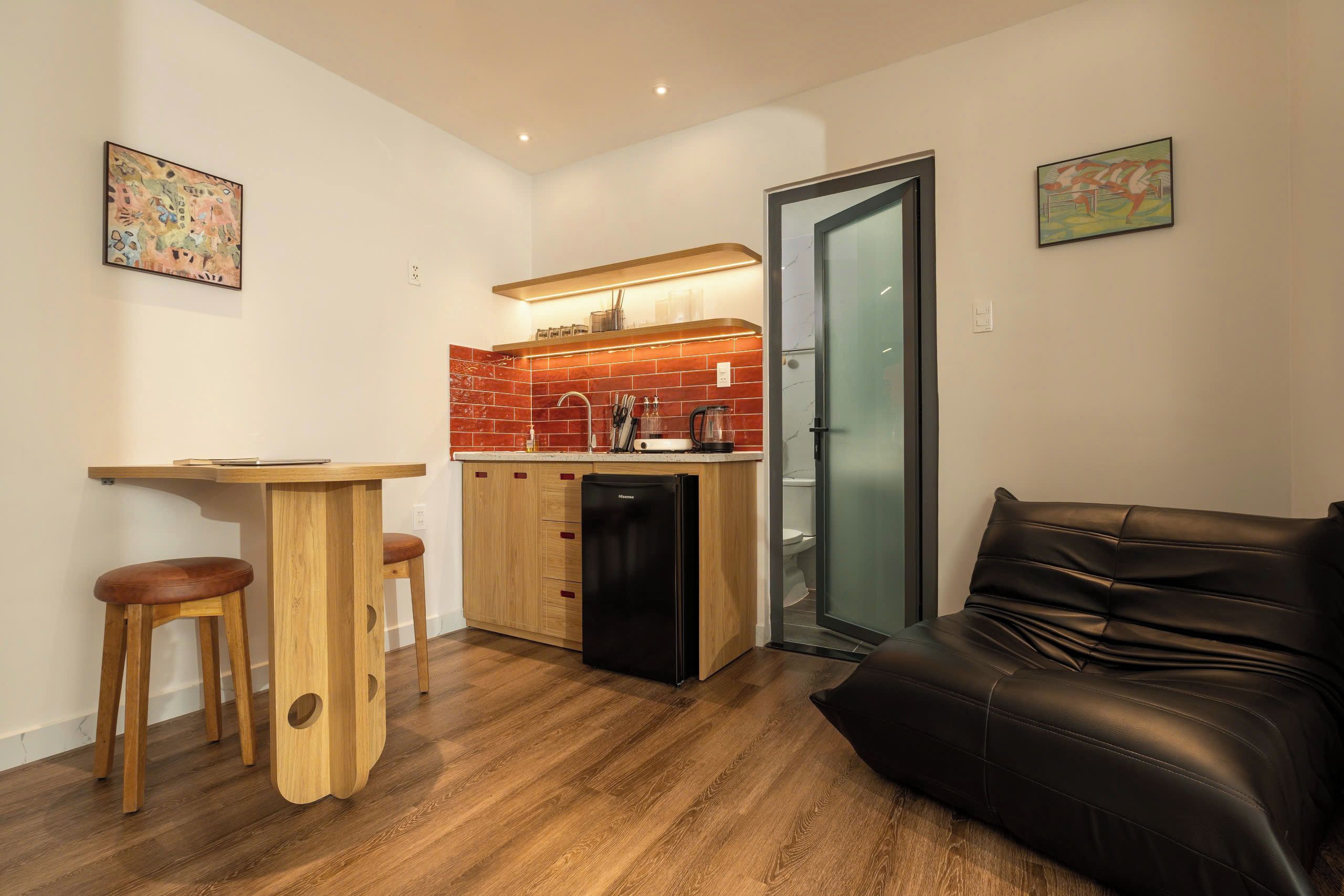Un espace de vie compact comprenant un coin cuisine, un coin repas avec des tabourets et un canapé en cuir.