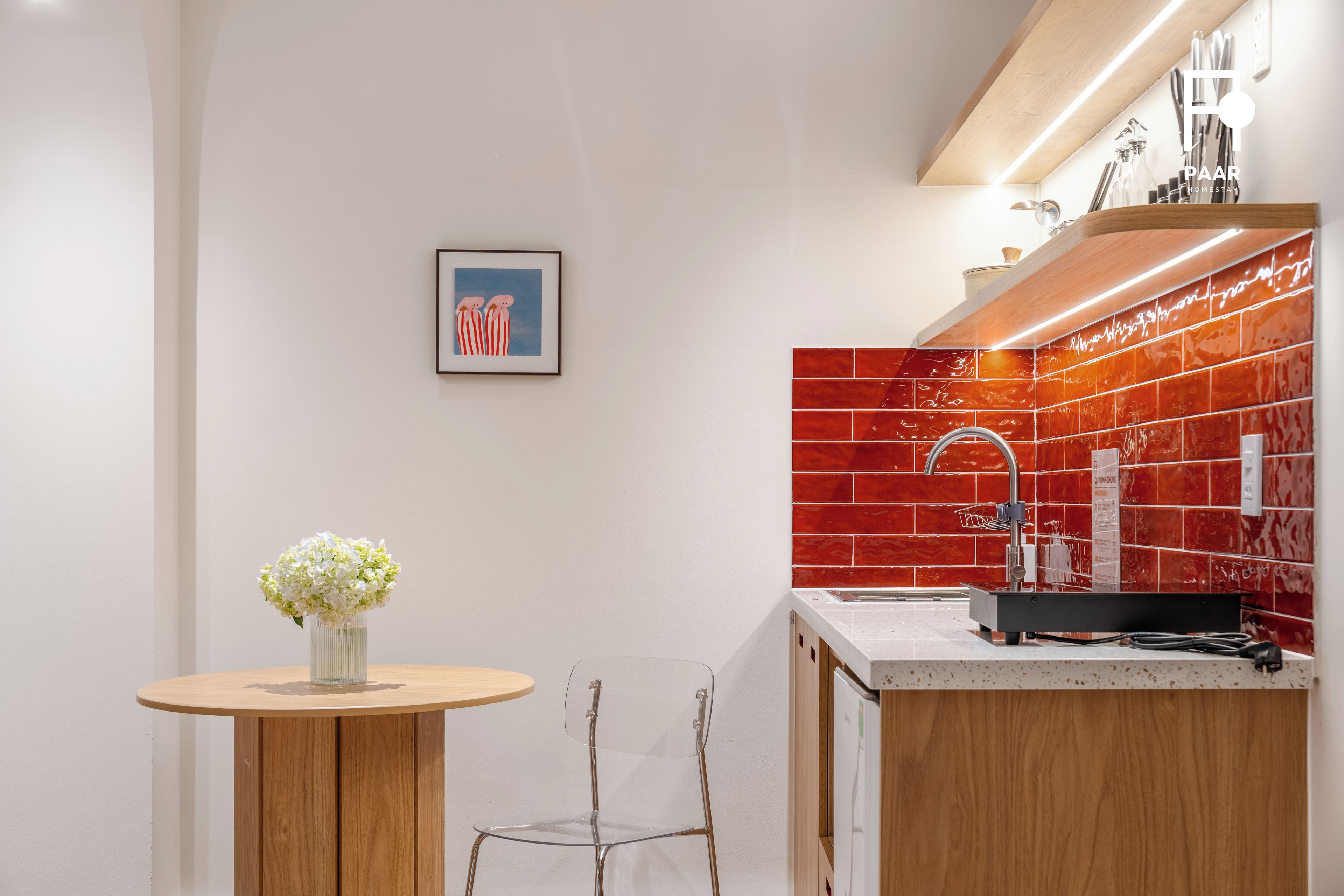 Une cuisine moderne avec un crédence rouge, un évier en acier inoxydable et une table à manger en bois sur laquelle est posé un vase de fleurs.