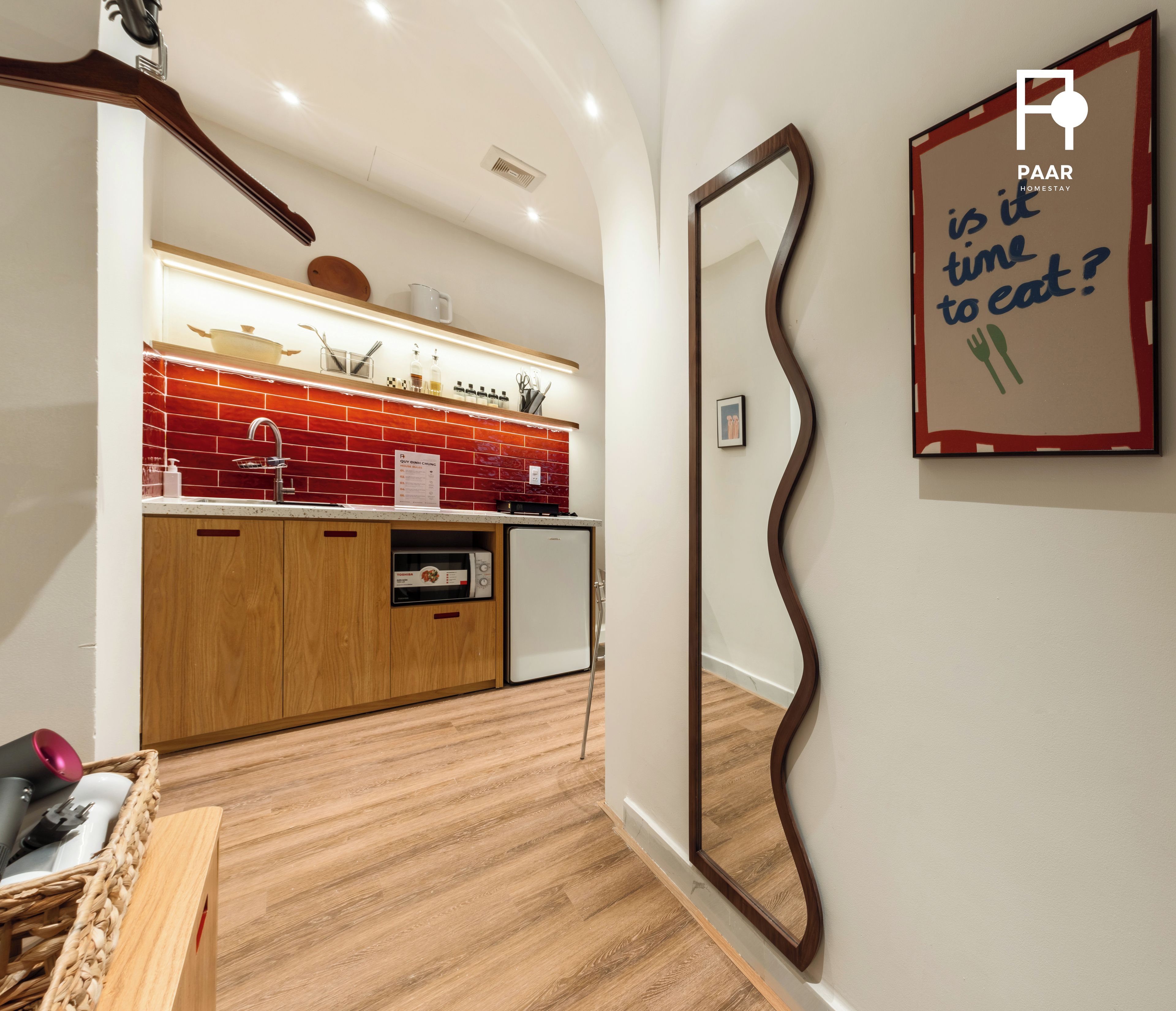 A modern kitchen with wooden cabinets, a red backsplash, and a microwave.