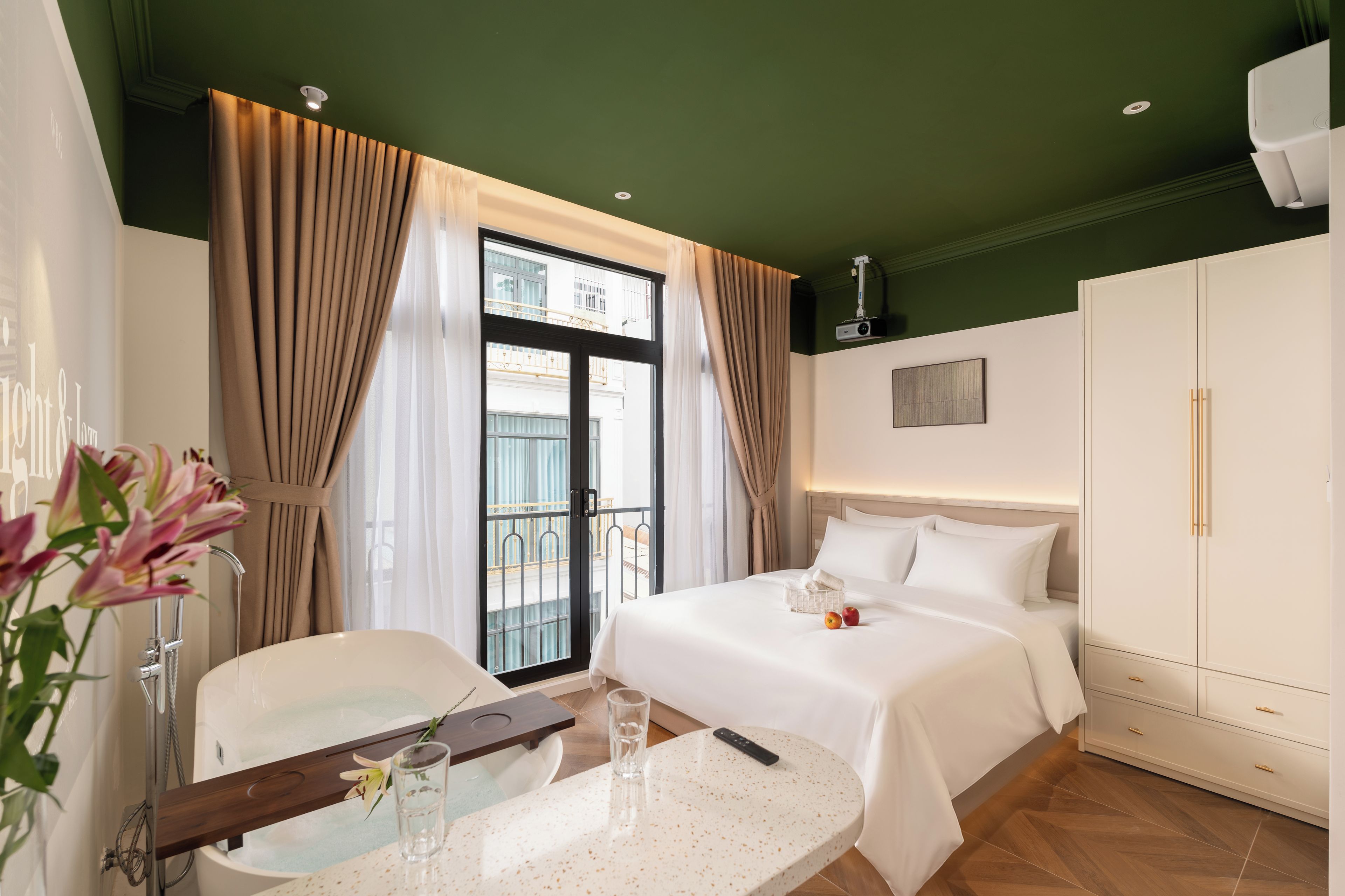 A hotel room with a bed, a desk with a chair, a bathroom, and a balcony with curtains.