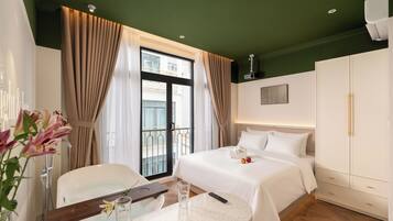 A hotel room with a bed, a desk with a chair, a bathroom, and a balcony with curtains.