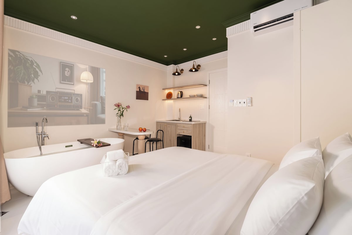 Une chambre d’hôtel moderne dotée d’un grand lit, d’une salle de bain séparée avec baignoire, d’une petite kitchenette et d’un coin repas.