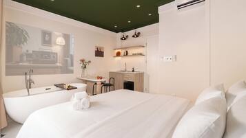 Een moderne hotelkamer met een groot bed, een aparte badkamer met bad, een klein kitchenette en een eethoek.