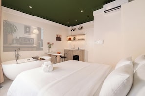 Une chambre d’hôtel moderne dotée d’un grand lit, d’une salle de bain séparée avec baignoire, d’une petite kitchenette et d’un coin repas.