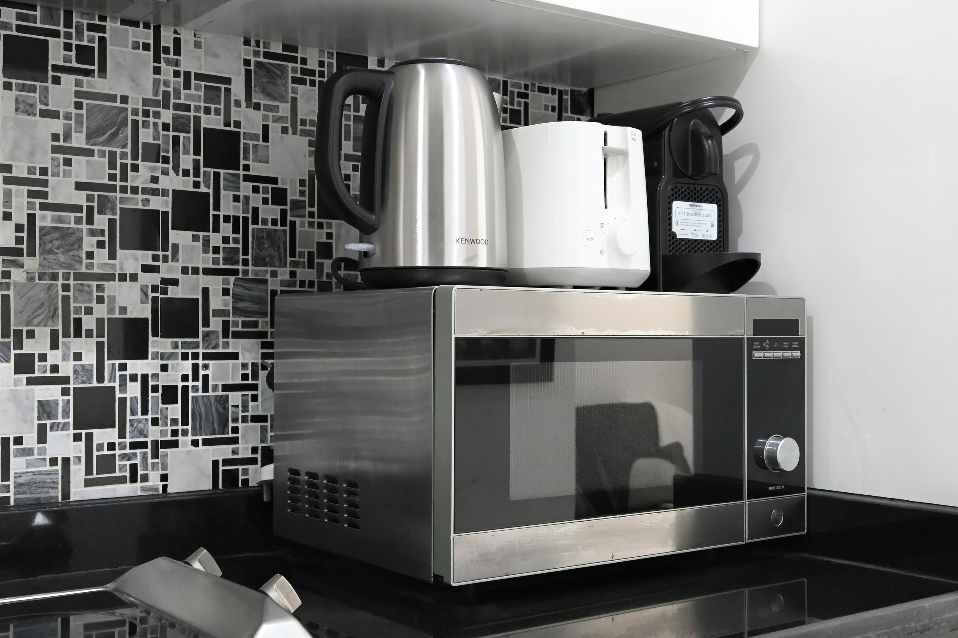 A modern kitchen with a stainless steel microwave oven, a kettle, and a coffee maker on the countertop.