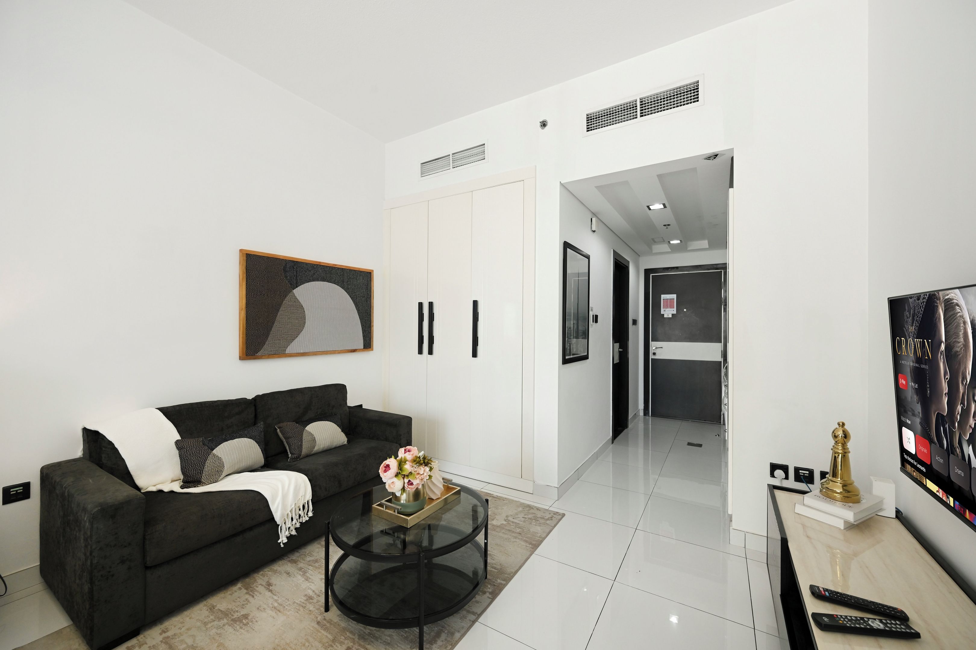 A modern living room with a black sofa, a glass coffee table, and a painting on the wall.