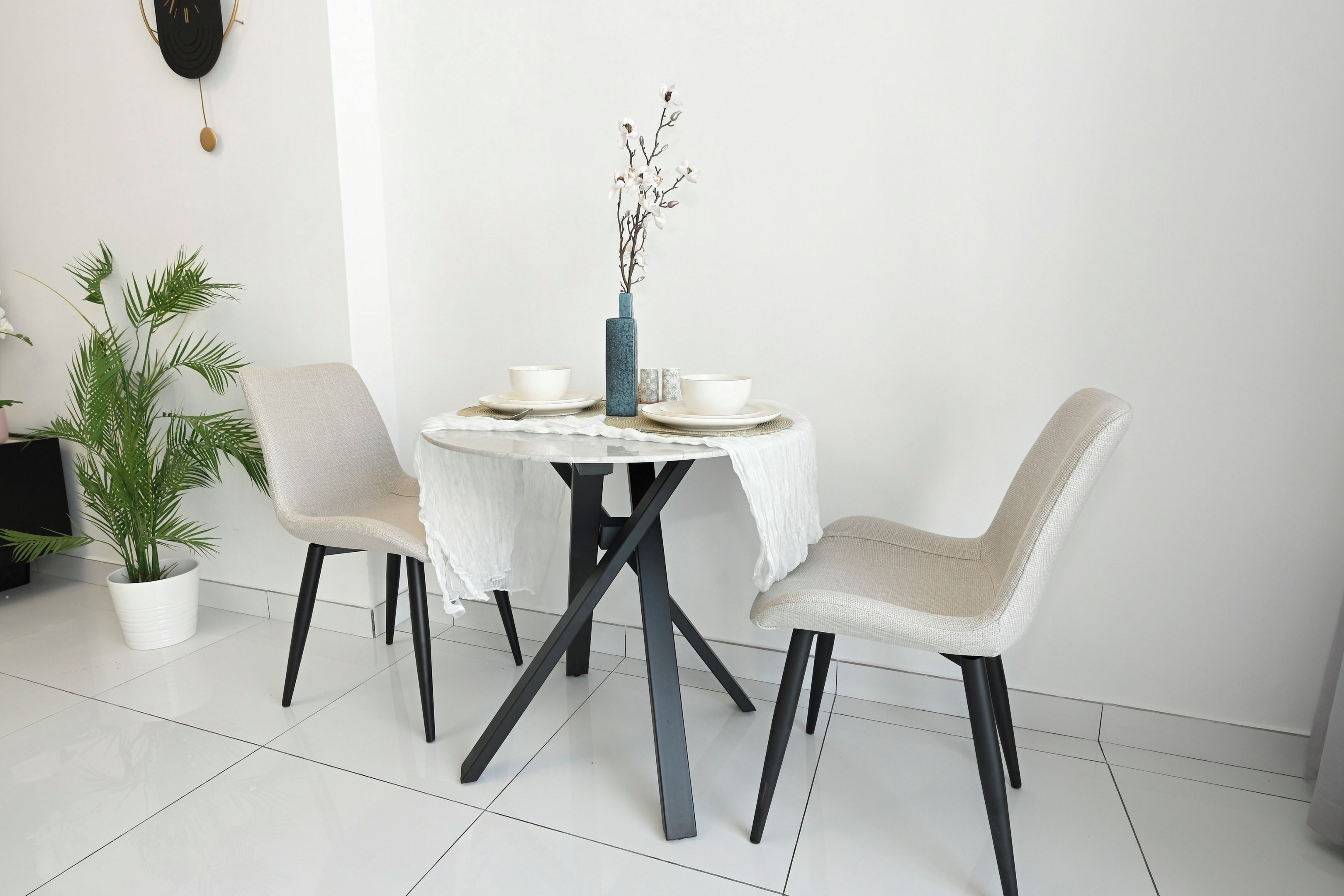 A dining area with a round table, two chairs, a vase with flowers, and a potted plant.