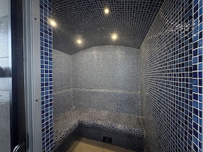 Een badkamer met betegelde wanden en vloer, een bankje en een deur.