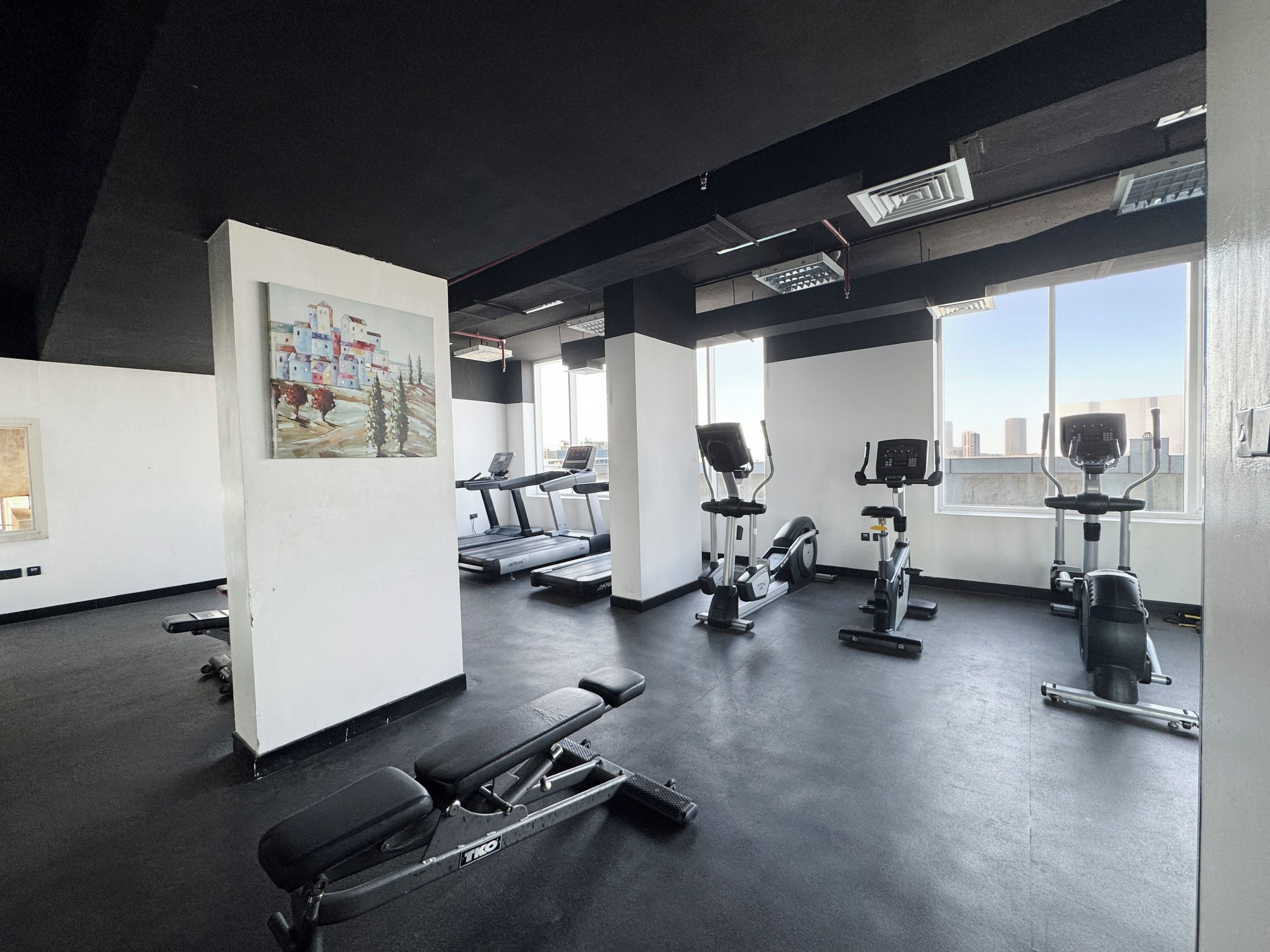 Une salle de sport équipée de tapis de course, de vélos elliptiques et d’une zone dédiée aux exercices de développé couché.