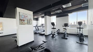 Une salle de sport équipée de tapis de course, de vélos elliptiques et d’une zone dédiée aux exercices de développé couché.