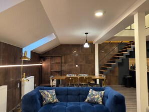 A modern living room with a blue sofa, a dining table, and a staircase. - Charming 2-Bedroom Apartment in Heart of Prague (Prague)