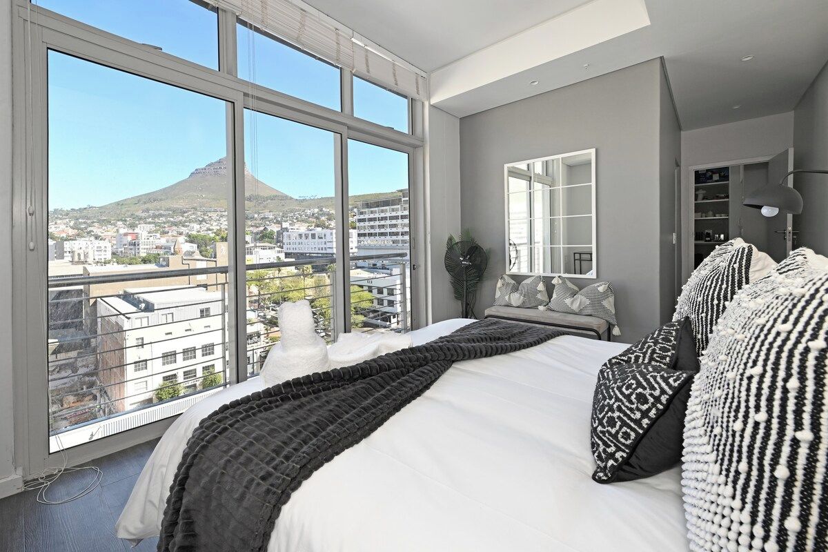 A bedroom with a large window, a bed with patterned pillows, and a view of a mountain.