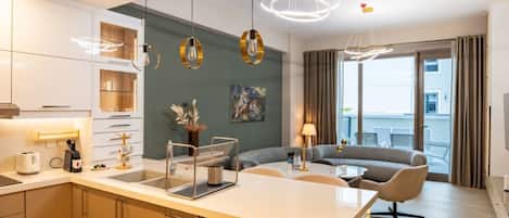Ein modernes Hotelzimmer mit Küchenzeile, Esstisch, einer Couch und einem großen Fenster mit Vorhängen.