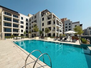 A modern residential building with a swimming pool, outdoor seating, and a clear sky. - La Rive - Stylish 2 Bedroom Apartment (Dubai)