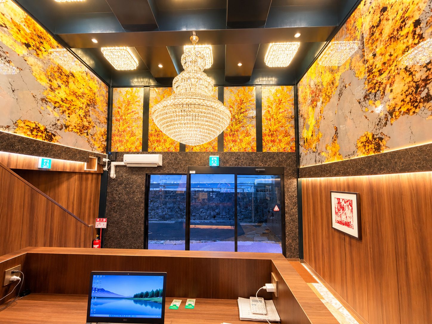A reception area with a wooden desk, a computer monitor, a telephone, and a chandelier.