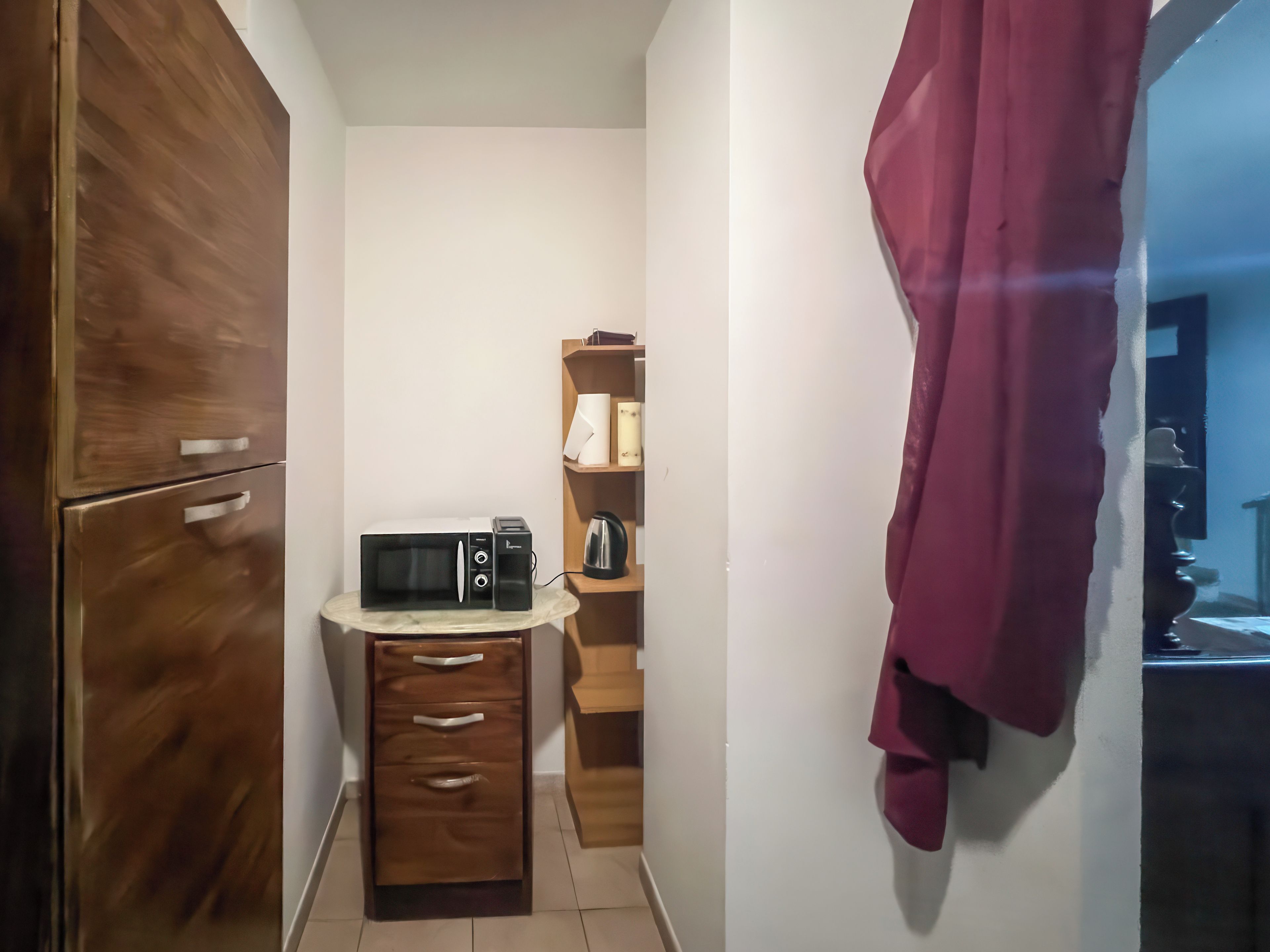 Eine kompakte Küche mit einer Mikrowelle, einem kleinen Schrank und einem Holzregal mit Küchenutensilien.