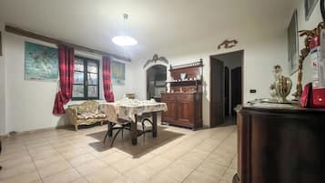 Un área de comedor con una mesa puesta para dos, un mueble de madera con adornos y una cortina roja.