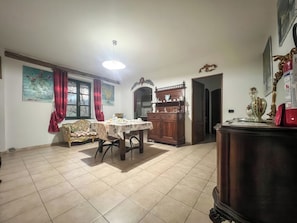 A dining area with a table set for two, a wooden cabinet with decorative items, and a red curtain.