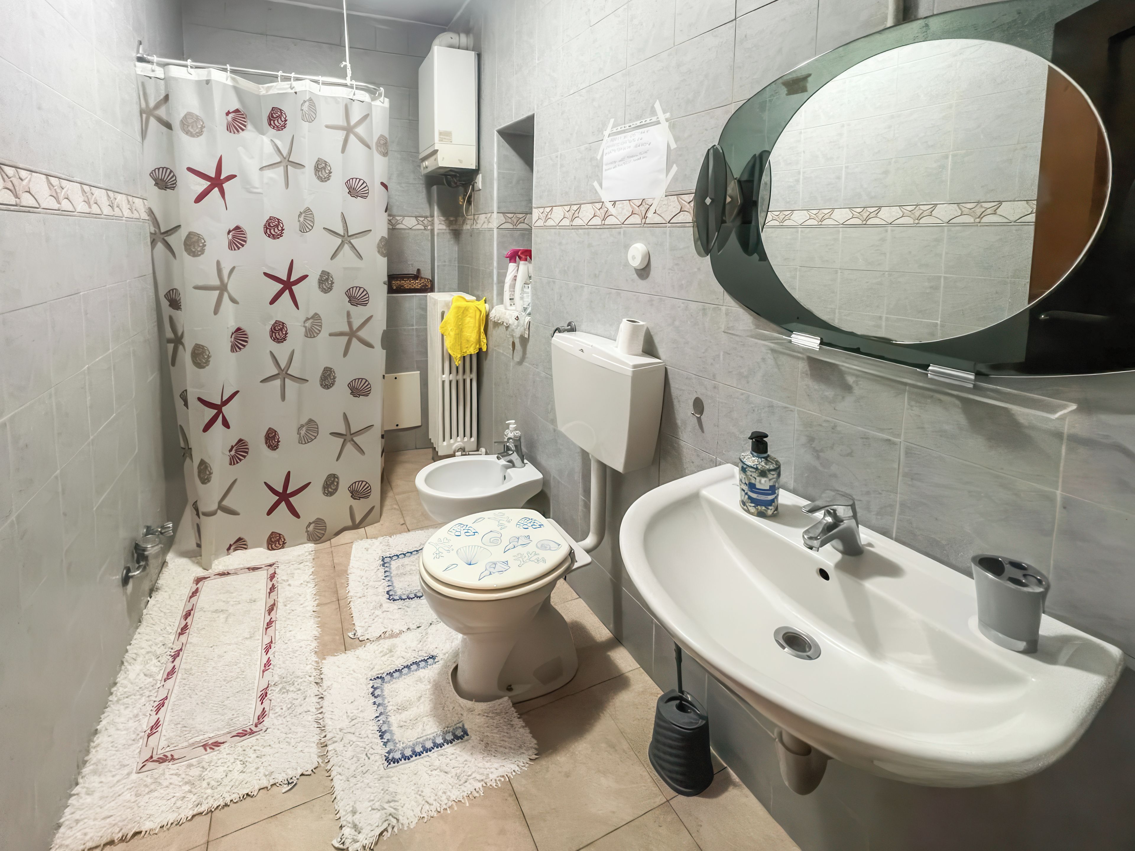 Un baño con inodoro, bidé, lavabo y cortina de ducha con estampado de estrellas de mar.
