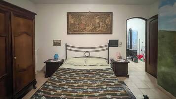 Un dormitorio con cama, mesita de noche, cómoda, un cuadro en la pared y una puerta que da a otra habitación.