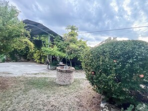 Un jardín con una jardinera de piedra, un banco y una estructura cubierta.