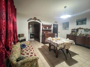 Ein Essbereich mit Tisch für zwei Personen, einer Couch, einem Schrank und einer Küche im Hintergrund.