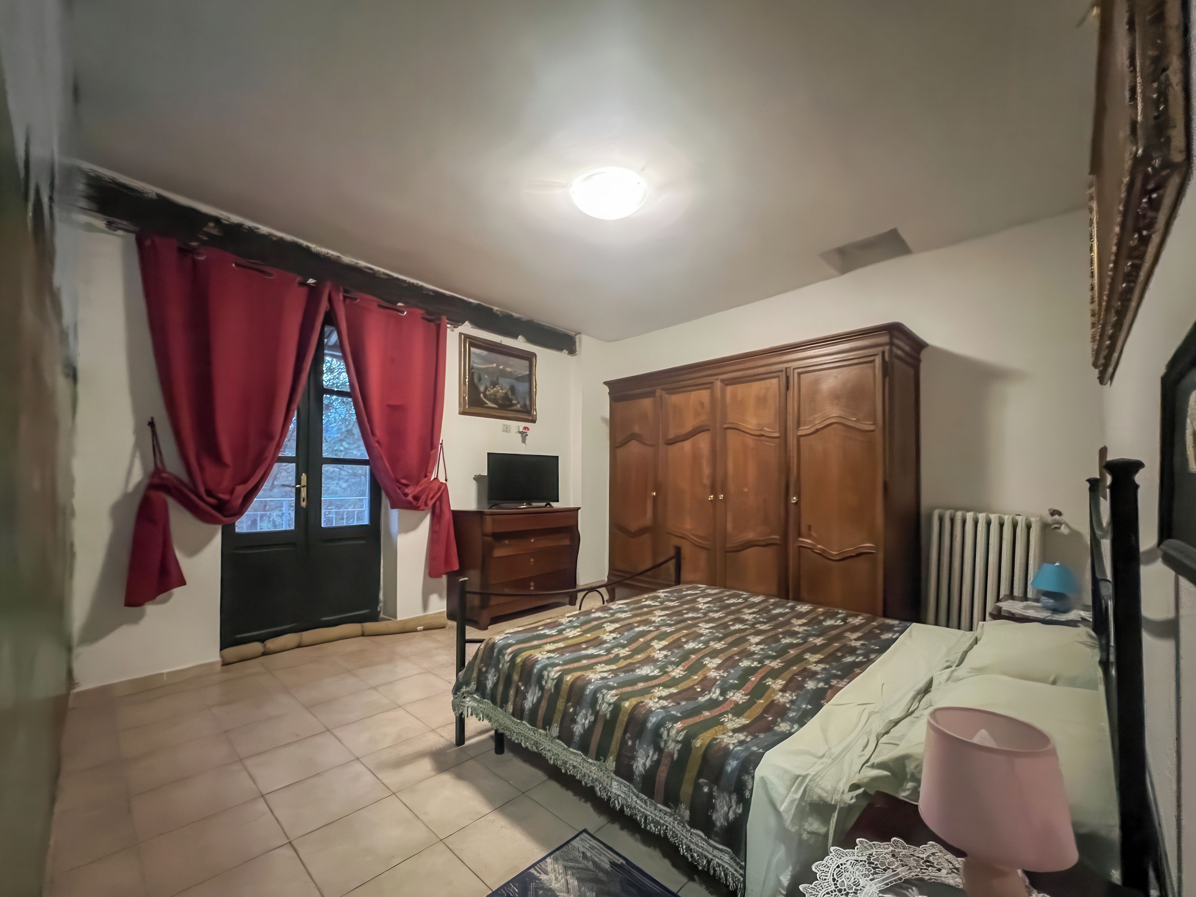 A bedroom with a bed, a dresser, a television, a wardrobe, and a window with curtains.
