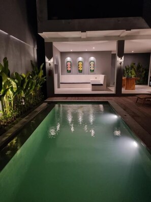 A pool area with a reception desk, a seating area, and a wall with decorative elements. - Agusta Villas Ungasan (Denpasar)