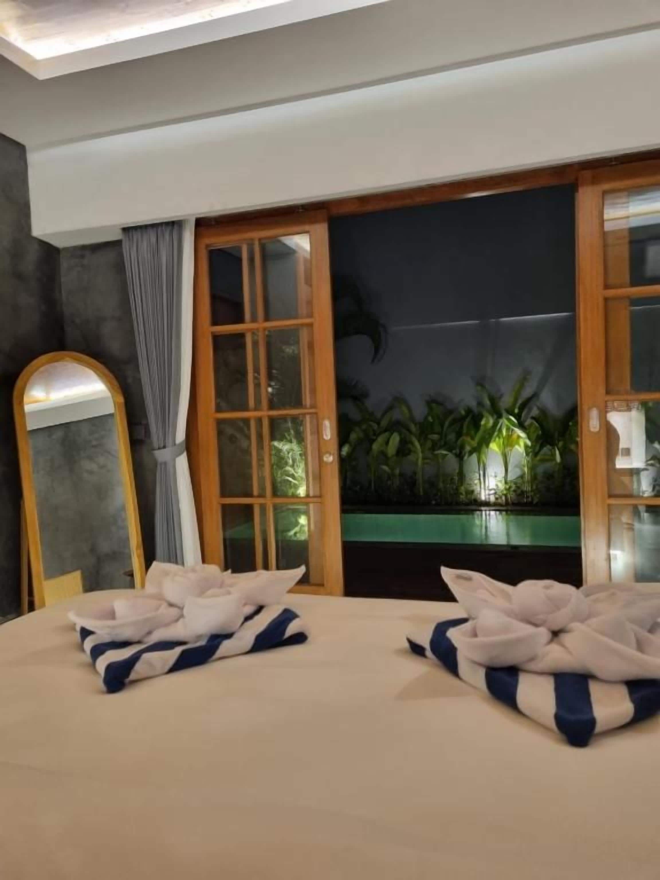 Habitación de hotel con cama, espejo y vistas a zonas verdes a través de un ventanal corredero.